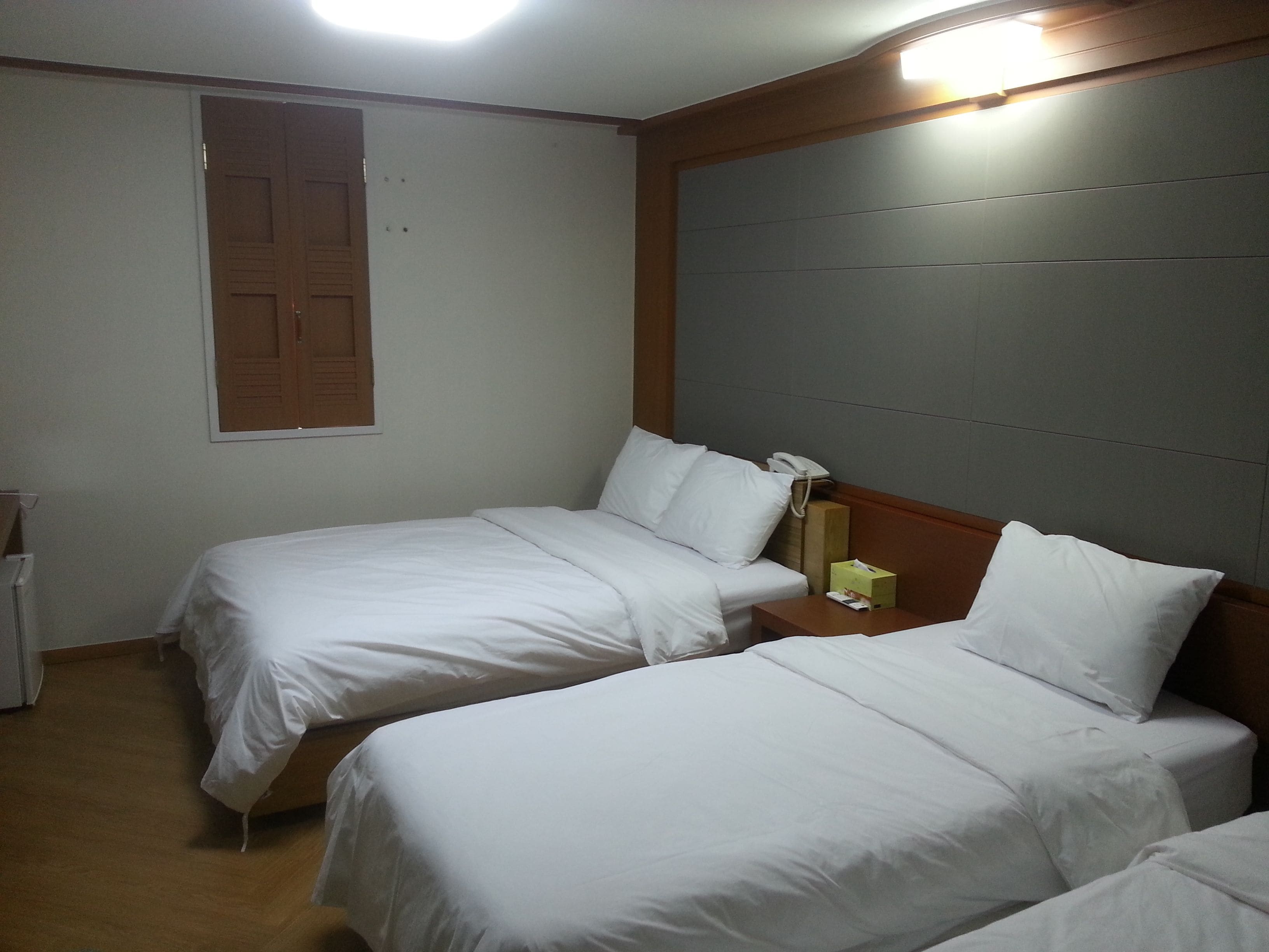 A hotel room with two single beds, a wooden headboard, a bedside table with a lamp, and a telephone.