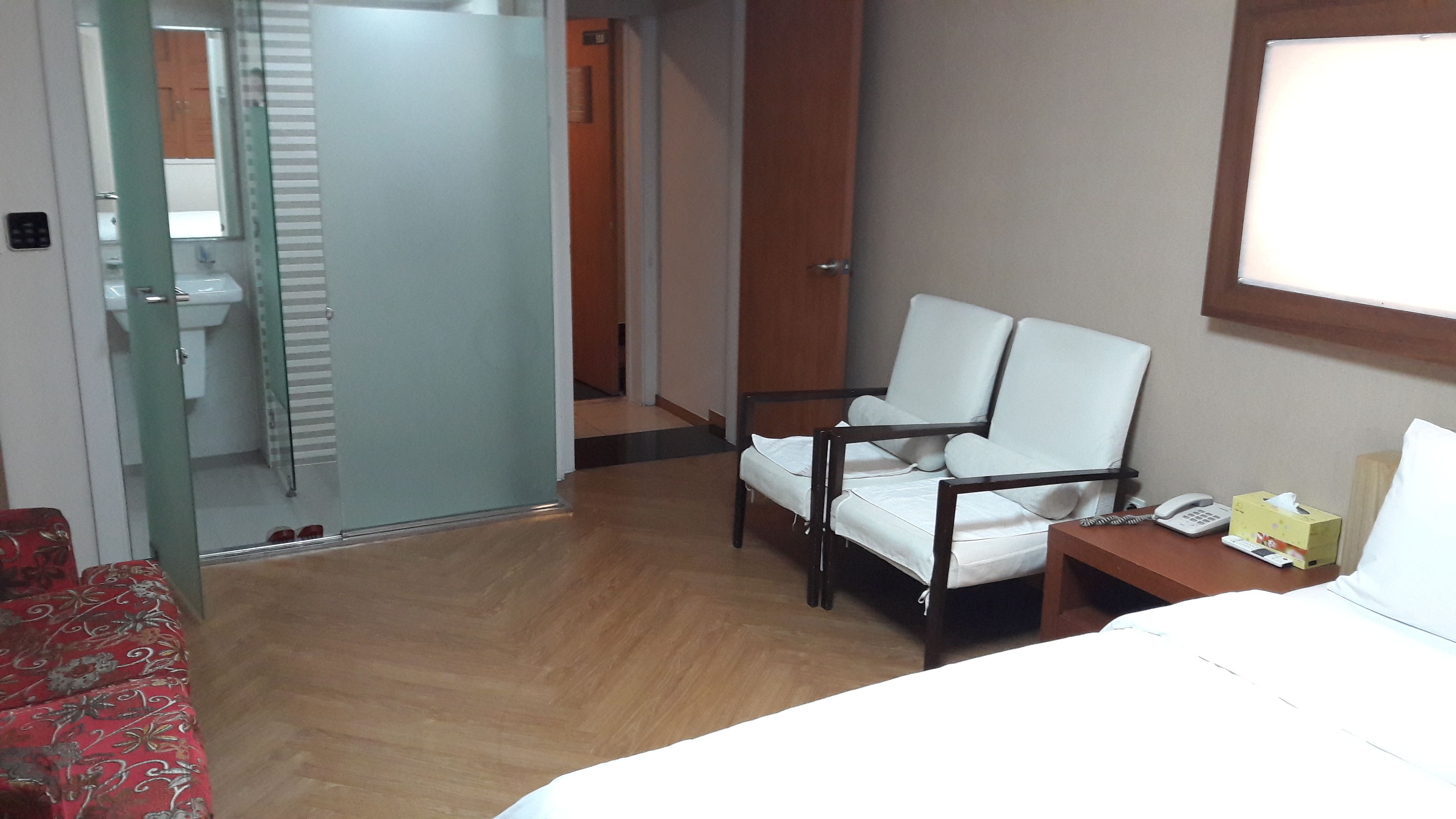 Une chambre d’hôtel avec un lit, une chaise, une table de chevet avec un téléphone, une boîte de mouchoirs et un miroir.