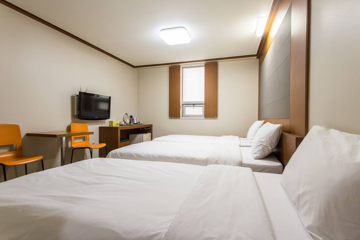 A hotel room with two beds, a desk, a chair, a television, and a window.