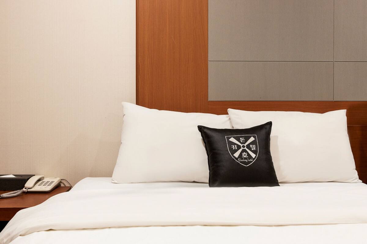 A hotel room with a neatly made bed, a nightstand with a telephone, and a pillow with a logo.
