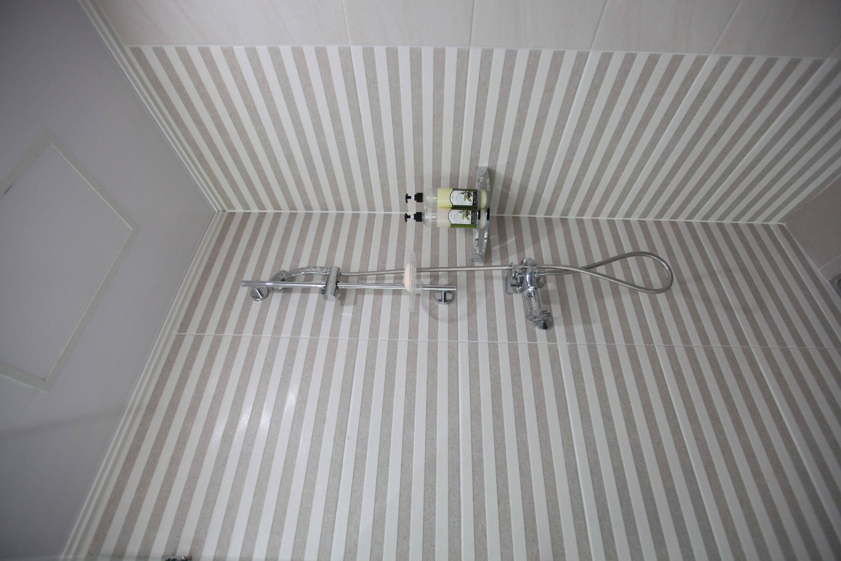 A shower area with a striped tile wall, a handheld showerhead, and a wall-mounted faucet.