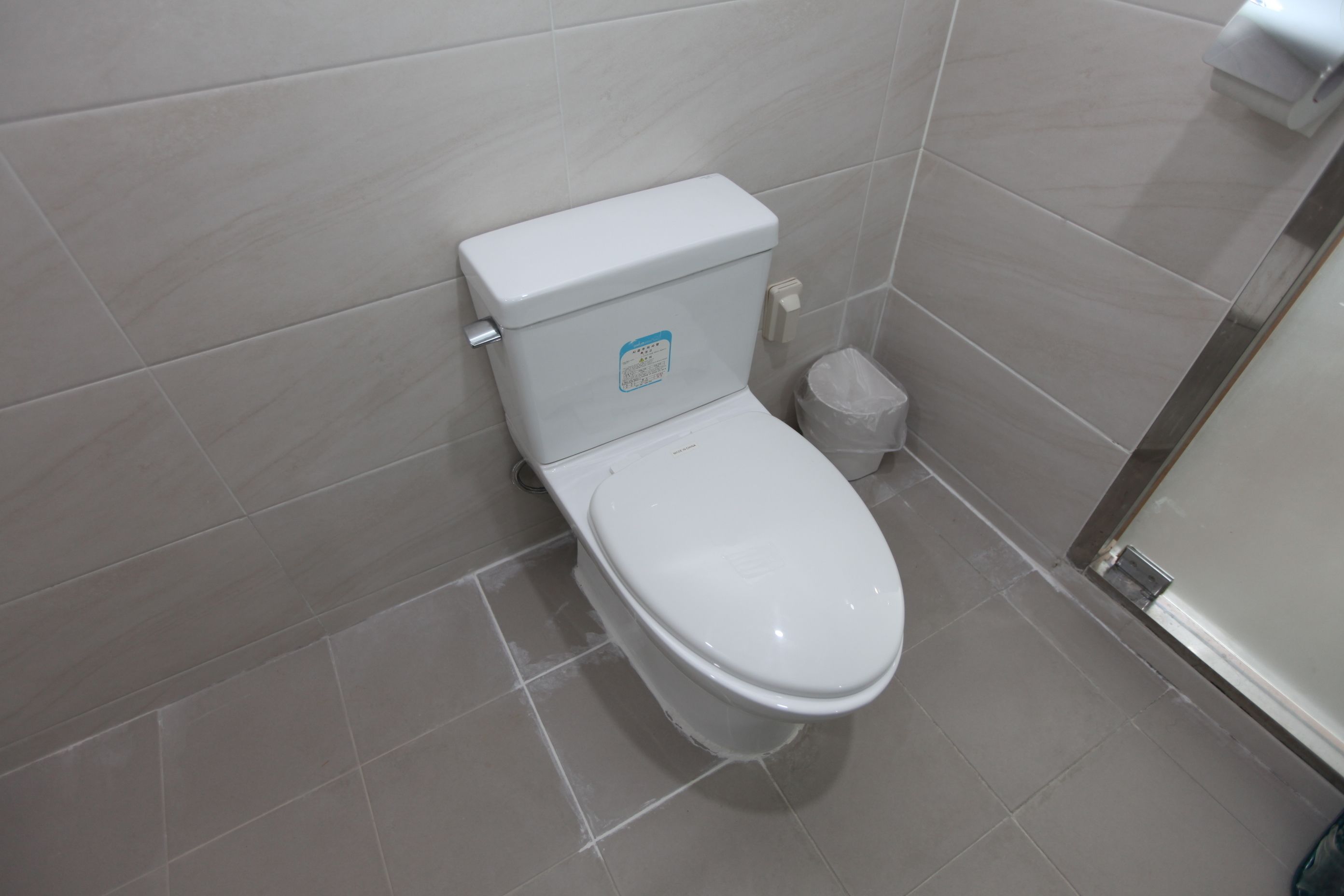 A modern bathroom with a white toilet, a trash bin, and a shower area.