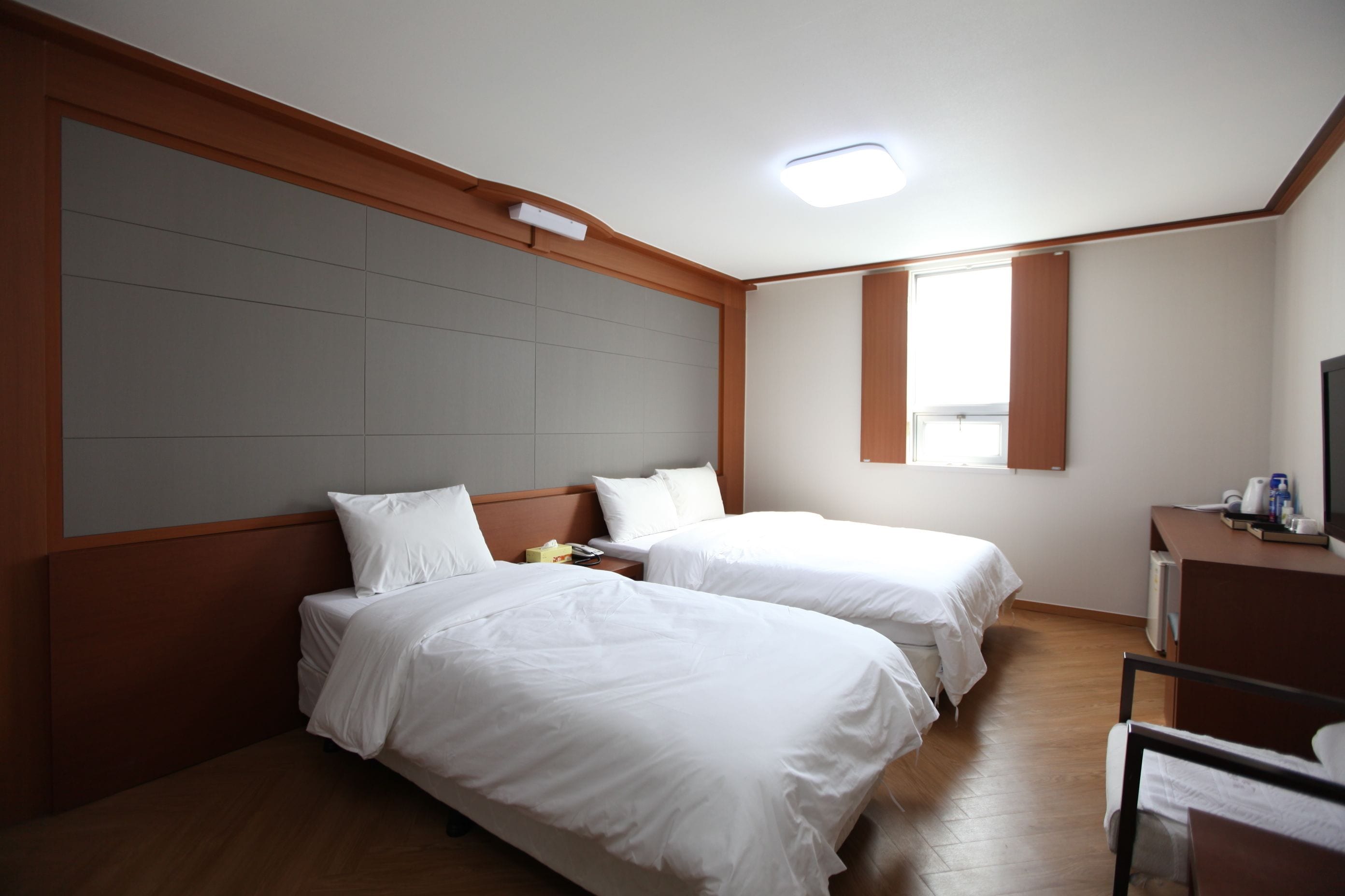 A hotel room with two beds, a wooden headboard, a desk with a chair, and a window.