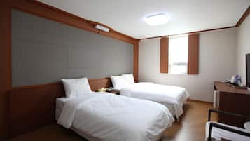 A hotel room with two beds, a wooden headboard, a desk with a chair, and a window.