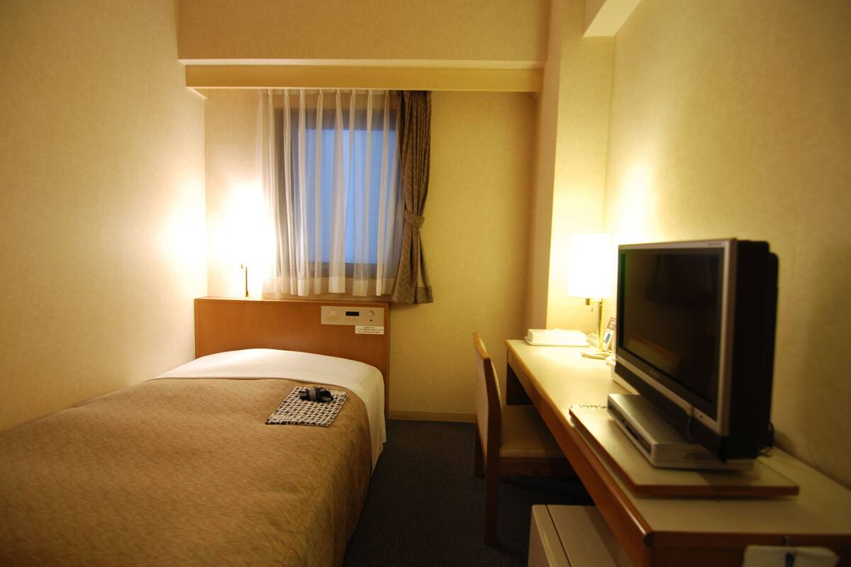 A hotel room with a bed, a desk, a television, and a window with curtains.