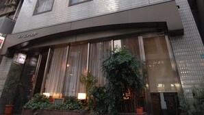 A modern building with a glass facade, large windows, and a green sign indicating a business. - Hotel New Star Ikebukuro (Tokyo)