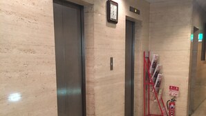 A hallway with two elevators, a clock, and a fire extinguisher. - Hotel New Star Ikebukuro (Tokyo)