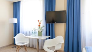 Ein Hotelzimmer mit an der Wand montiertem Fernseher, einem Tisch mit zwei Stühlen, einer Vase mit Blumen und einer Lampe.