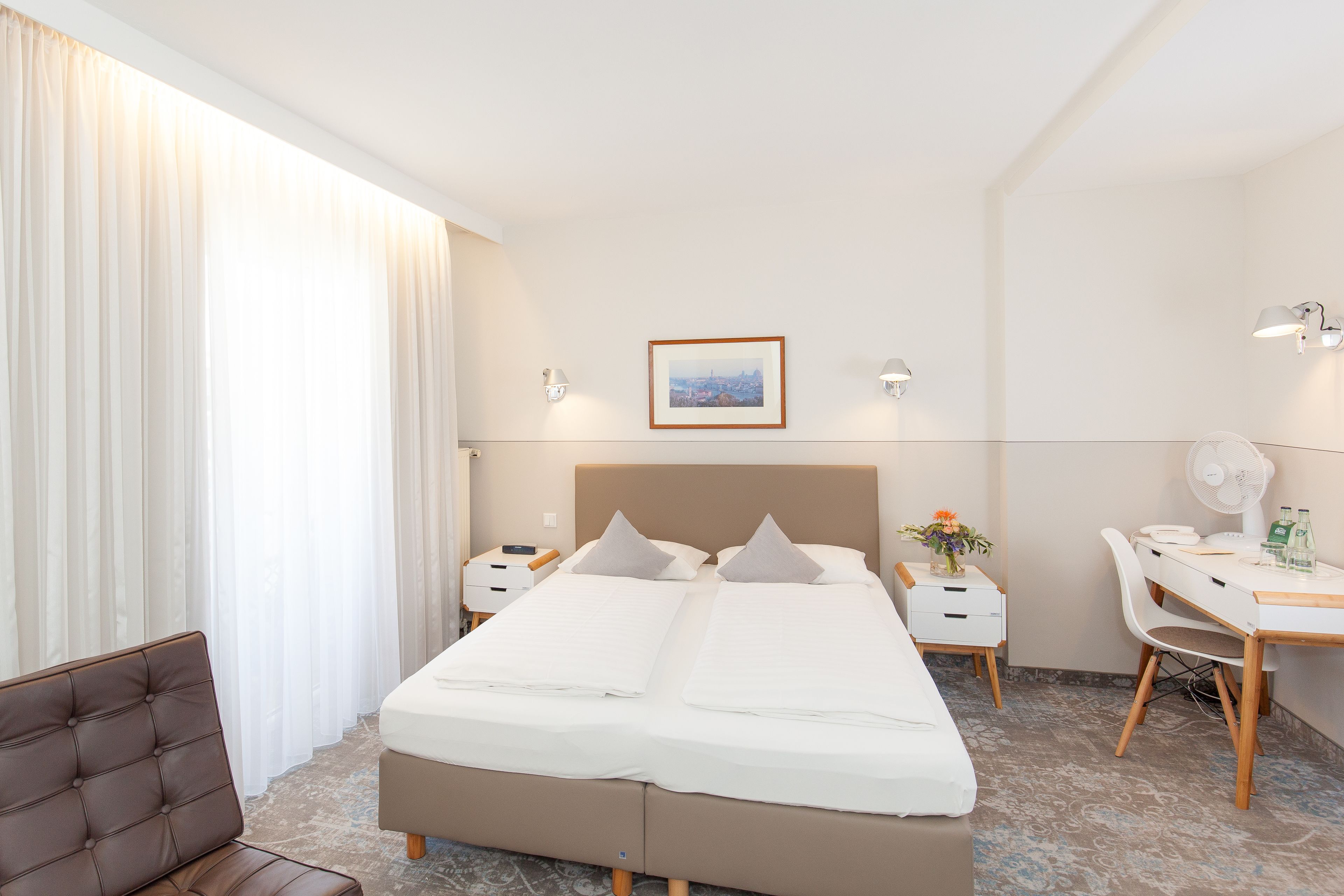 A hotel room with a large bed, a desk, a chair, and a window with curtains.