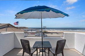 Un balcon avec deux chaises et une table, donnant sur une plage et l’océan.