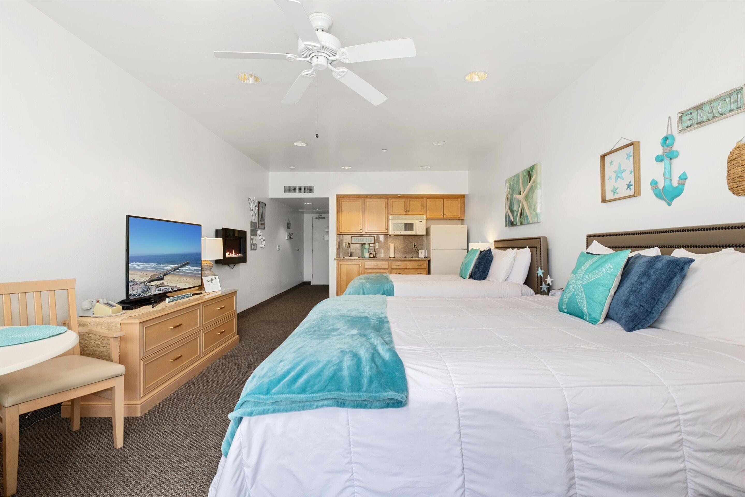 A hotel room with a large bed, a desk with a chair, a television, and a kitchenette.
