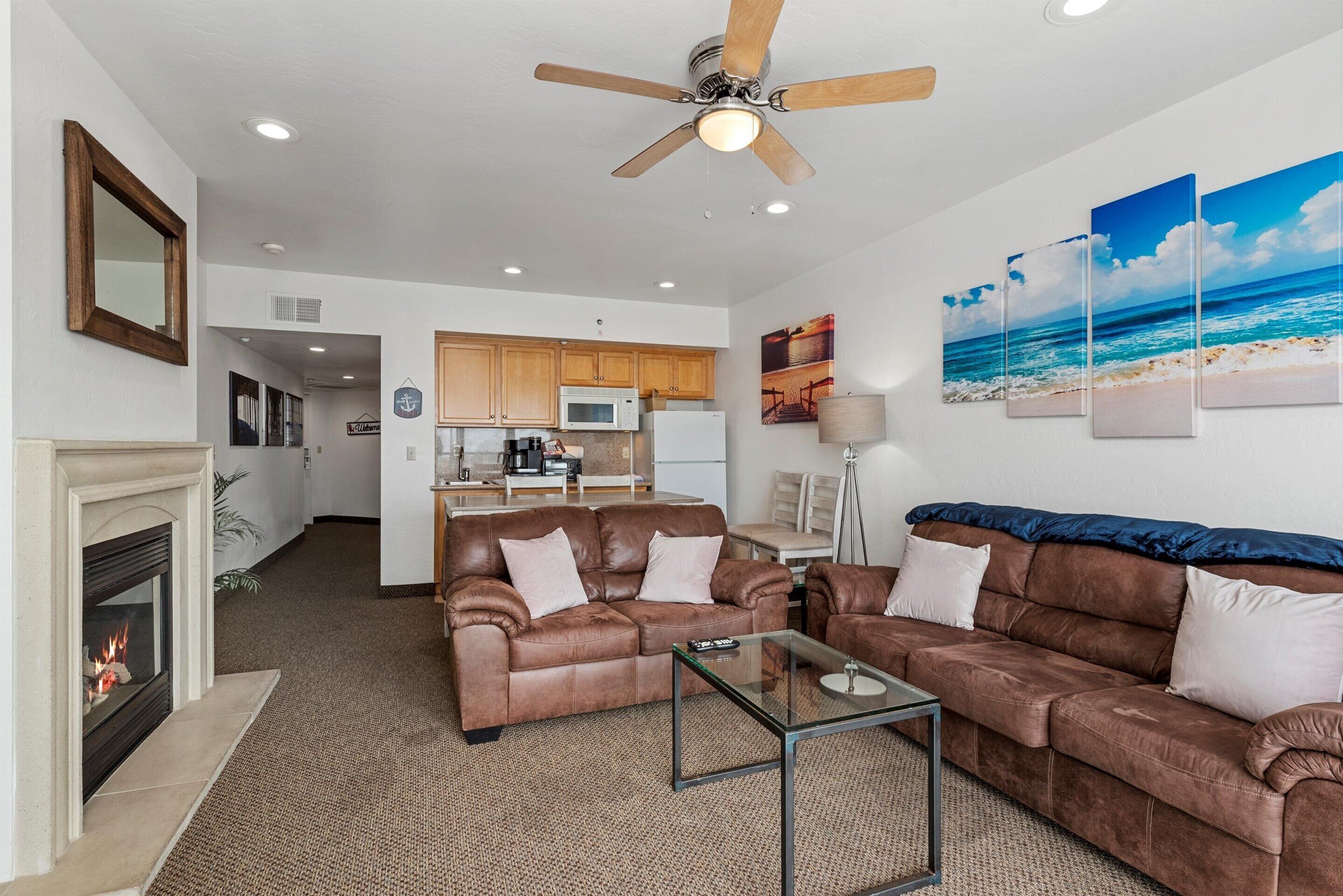 A living room with a fireplace, brown leather sofas, a glass coffee table, and a ceiling fan.