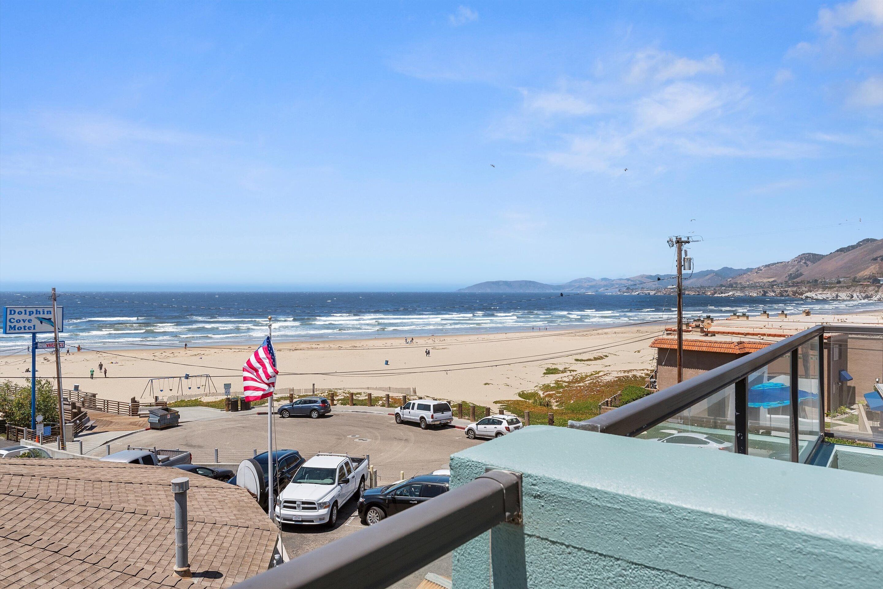 A view of a beach with a parking lot, a Dolphin Cove Motel sign, and an American flag.