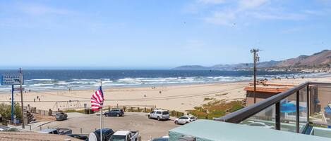 A view of a beach with a parking lot, a Dolphin Cove Motel sign, and an American flag.