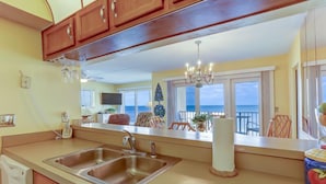 A kitchen with a double sink, wooden cabinets, a chandelier, and a view of the ocean through large windows. - Oceans of Amelia Condos (Fernandina Beach)