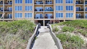 A multi-story hotel with balconies and a concrete pathway leading to the entrance. - Oceans of Amelia Condos (Fernandina Beach)