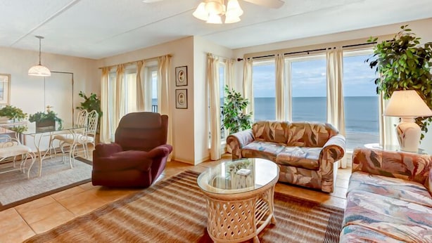 A living room with a view of the sea, a ceiling fan, a dining area with a table and chairs, and a sofa. - Oceans of Amelia Condos (Fernandina Beach)