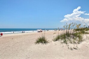 A beach with sand dunes, a clear sky, and a few beachgoers.