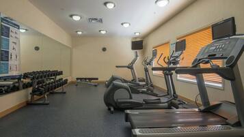 Une salle de sport équipée de tapis de course, de vélos elliptiques et d’une série d’haltères.