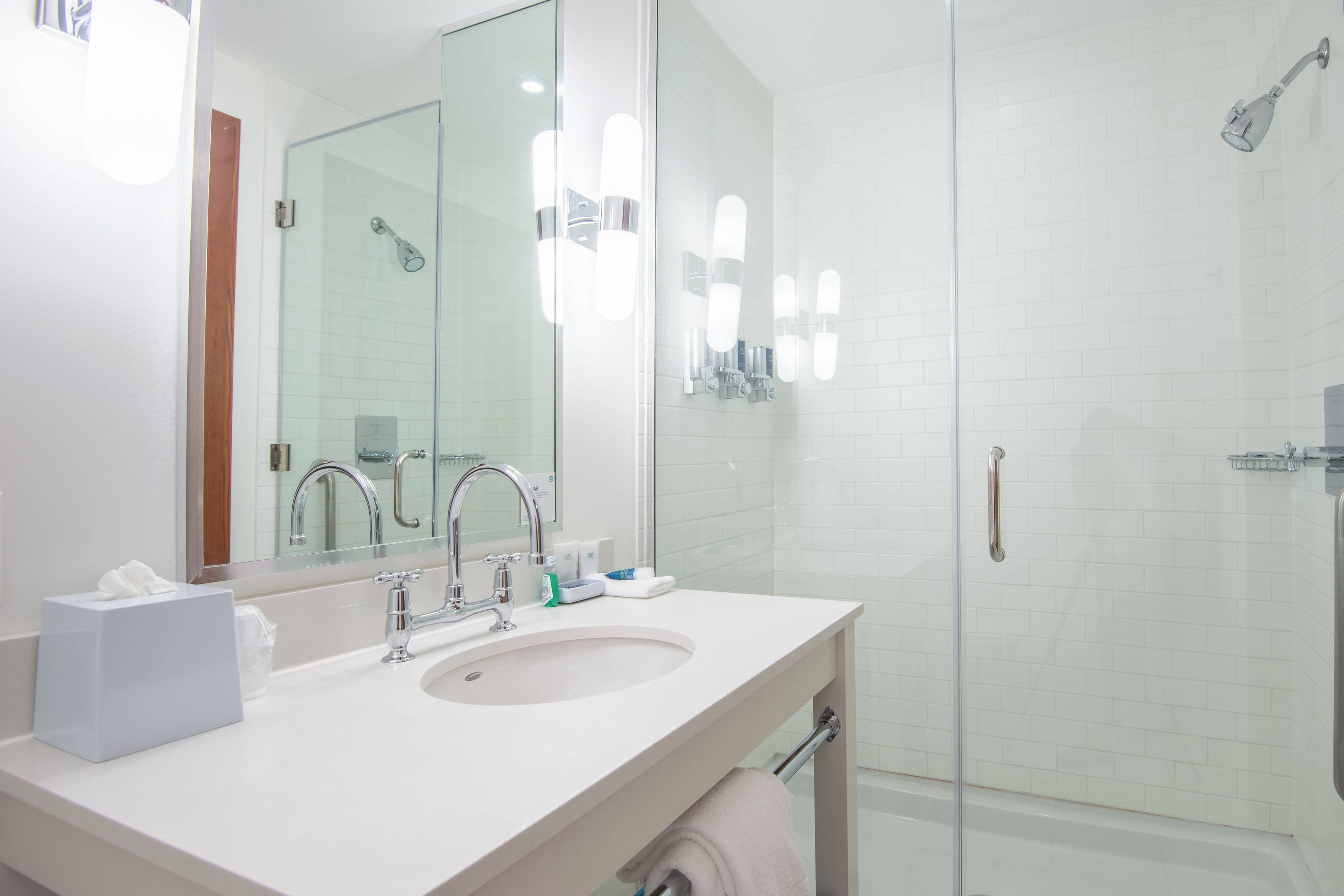 A modern bathroom with a sink, mirror, and glass shower enclosure.
