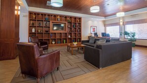 Un vaste espace de vie doté d’un plafond en bois, d’un grand téléviseur fixé sur une étagère en bois, de fauteuils en cuir, d’un canapé et d’une table basse.