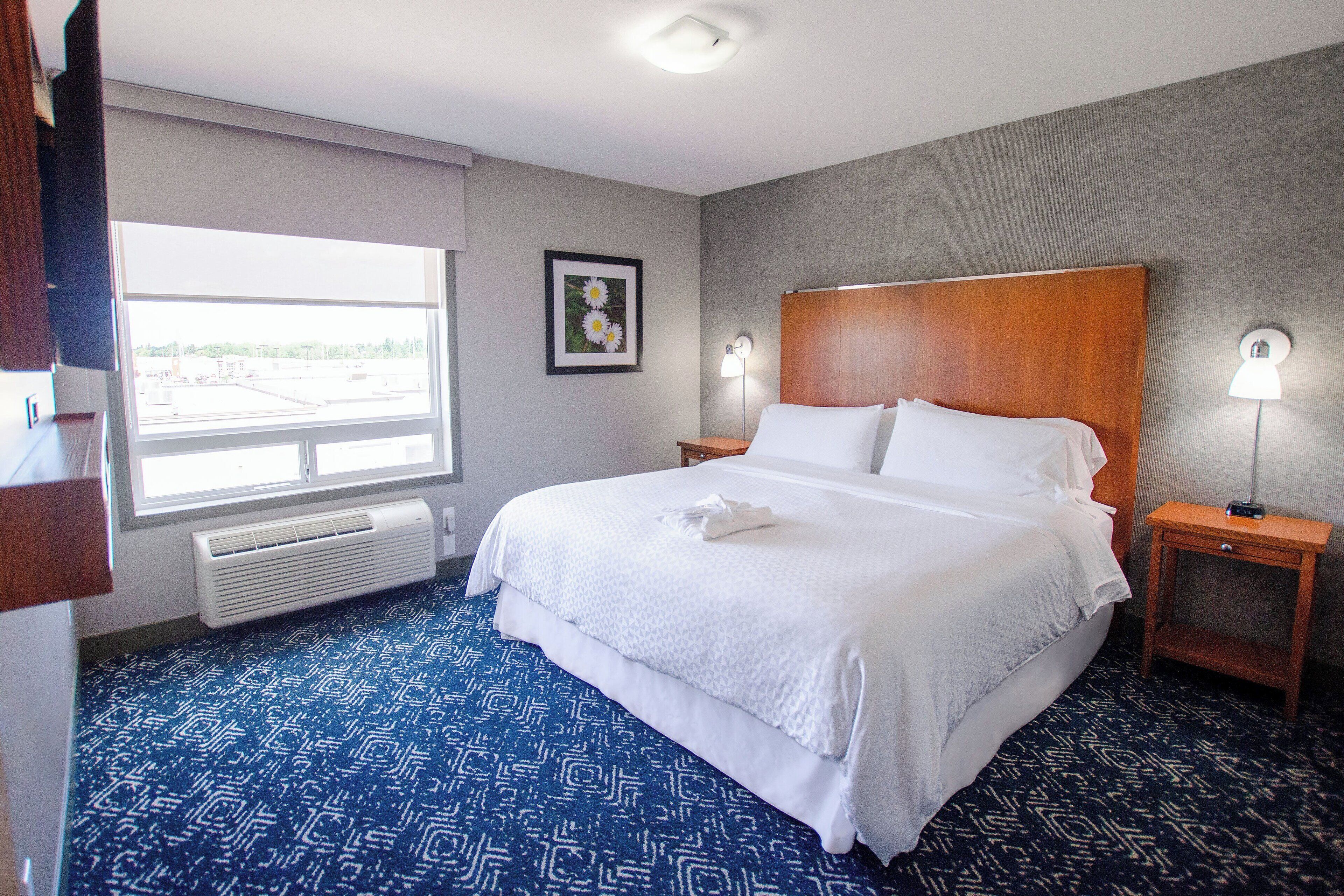 A hotel room with a large bed, two bedside tables with lamps, a window with a view, and a framed picture on the wall.