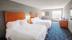 Une chambre d’hôtel avec deux lits, un bureau, une chaise, une lampe et une fenêtre donnant sur un beau paysage.