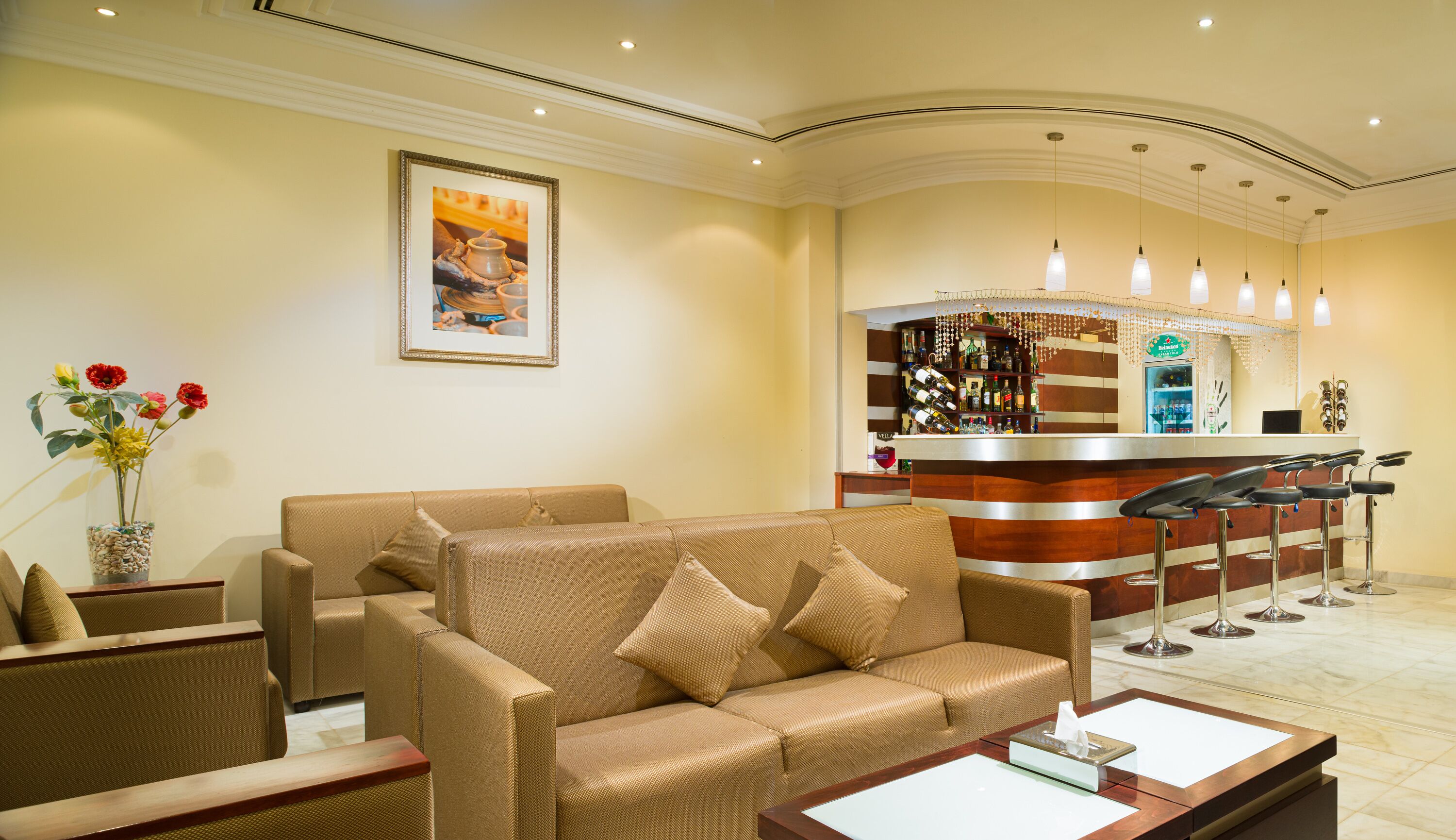 A hotel lobby with a sofa, armchairs, a bar area with stools, and a framed picture on the wall.