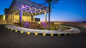 A building with a covered entrance, stone pillars, and a landscaped area with a palm tree. - Masira Island Resort (Masirah)