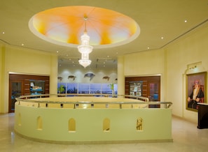 Un hall d’entrée doté d’un bar central circulaire, d’un lustre, d’un grand ventilateur de plafond et offrant une vue sur la mer par les fenêtres.