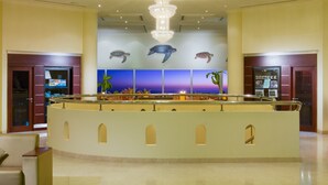 A lobby with a central reception desk, a large chandelier, a tiled floor with a circular pattern, and a wall with turtle murals. - Masira Island Resort (Masirah)
