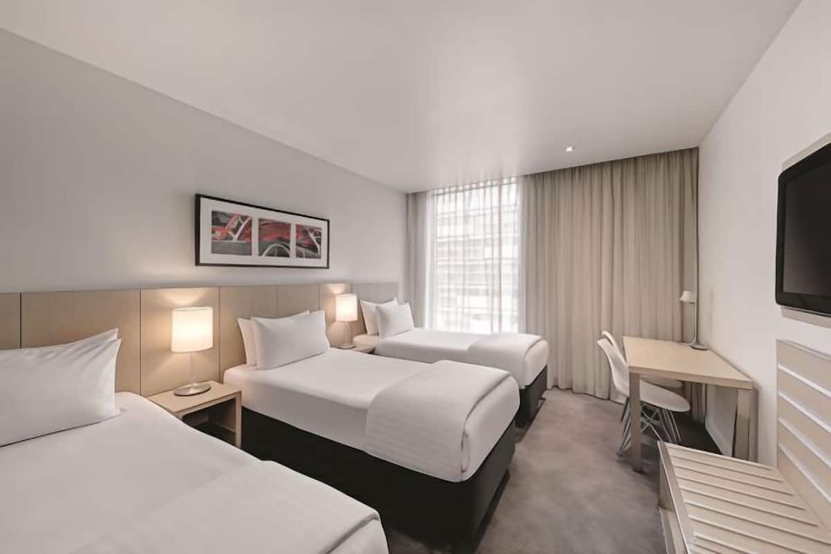 Ett hotellrum med två sängar, ett skrivbord, en TV och ett fönster med gardiner.