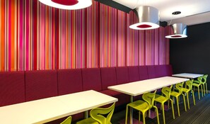 Ein modernes Restaurant mit gestreifter Wandgestaltung, roten Sitzflächen und grünen Stühlen.