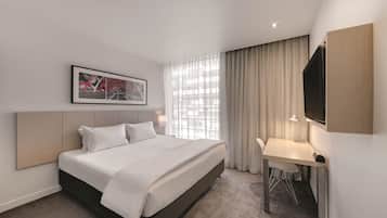 Ett hotellrum med en säng, ett skrivbord och ett stort fönster med gardiner.