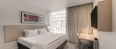 A hotel room with a bed, desk, and a large window with curtains.