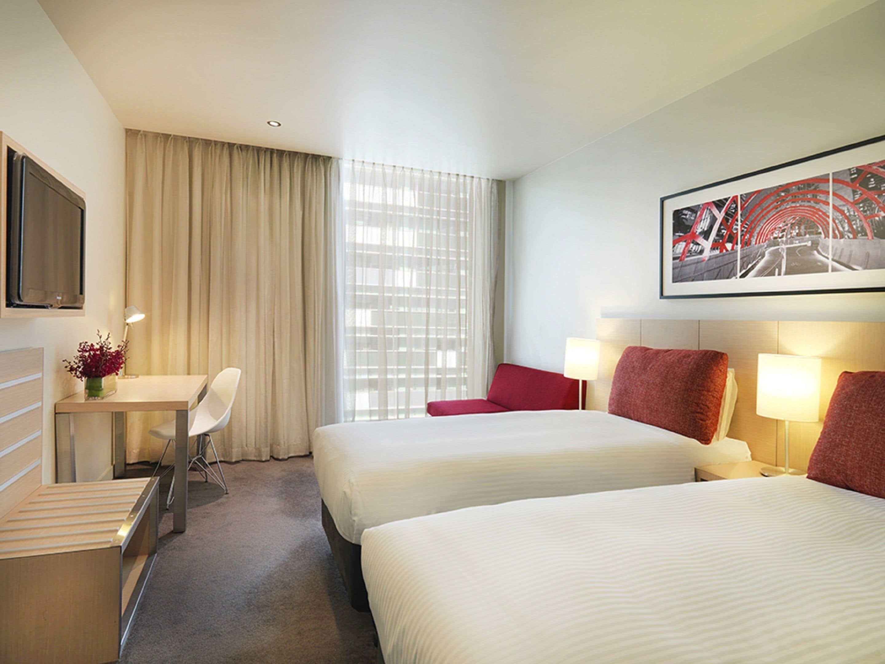 A hotel room with two beds, a desk, a chair, and a TV.