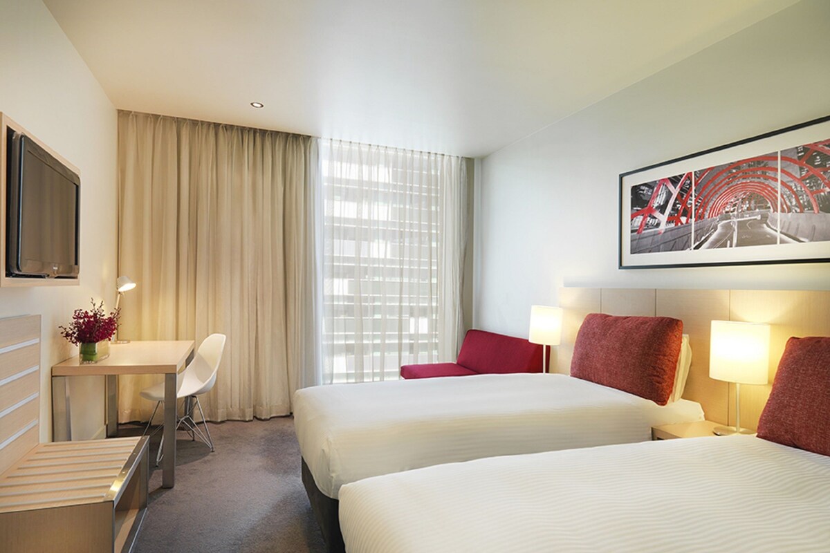 Een hotelkamer met twee bedden, een bureau, een stoel en een televisie.