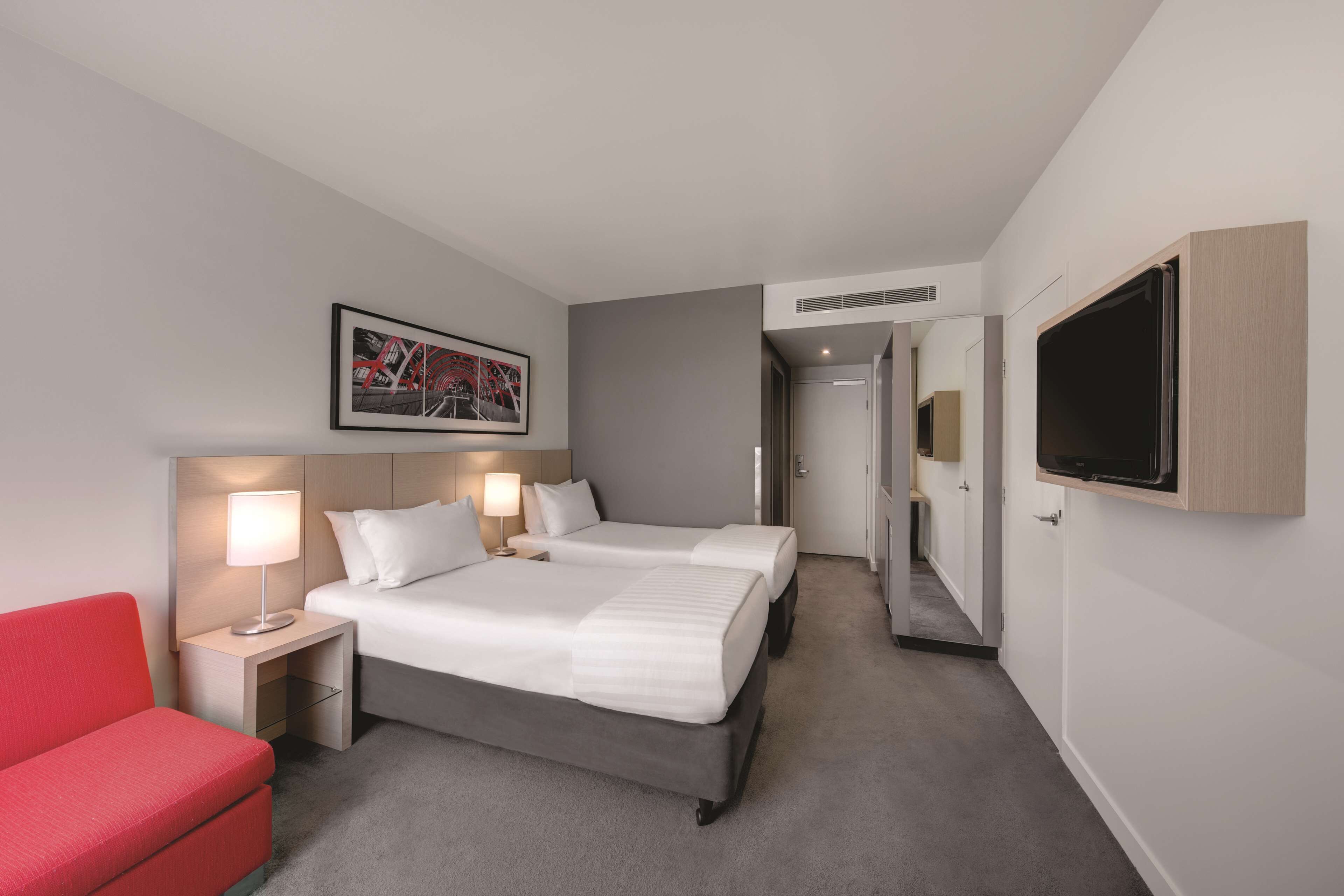 A hotel room with two beds, a red chair, a TV, and a framed picture on the wall.