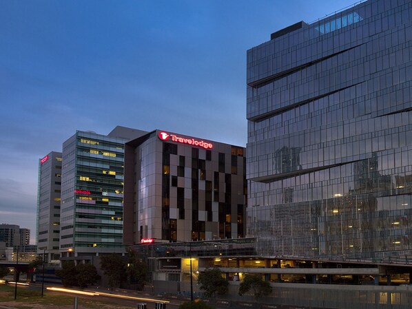 Een modern hotel met een opvallend Travelodge-bord, meerdere verdiepingen en een glazen gevel die de stadszicht weerspiegelt.