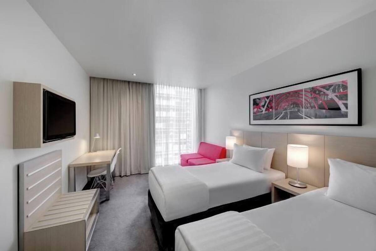 Ett hotellrum med två sängar, ett skrivbord, en stol, en TV och ett fönster med gardiner.