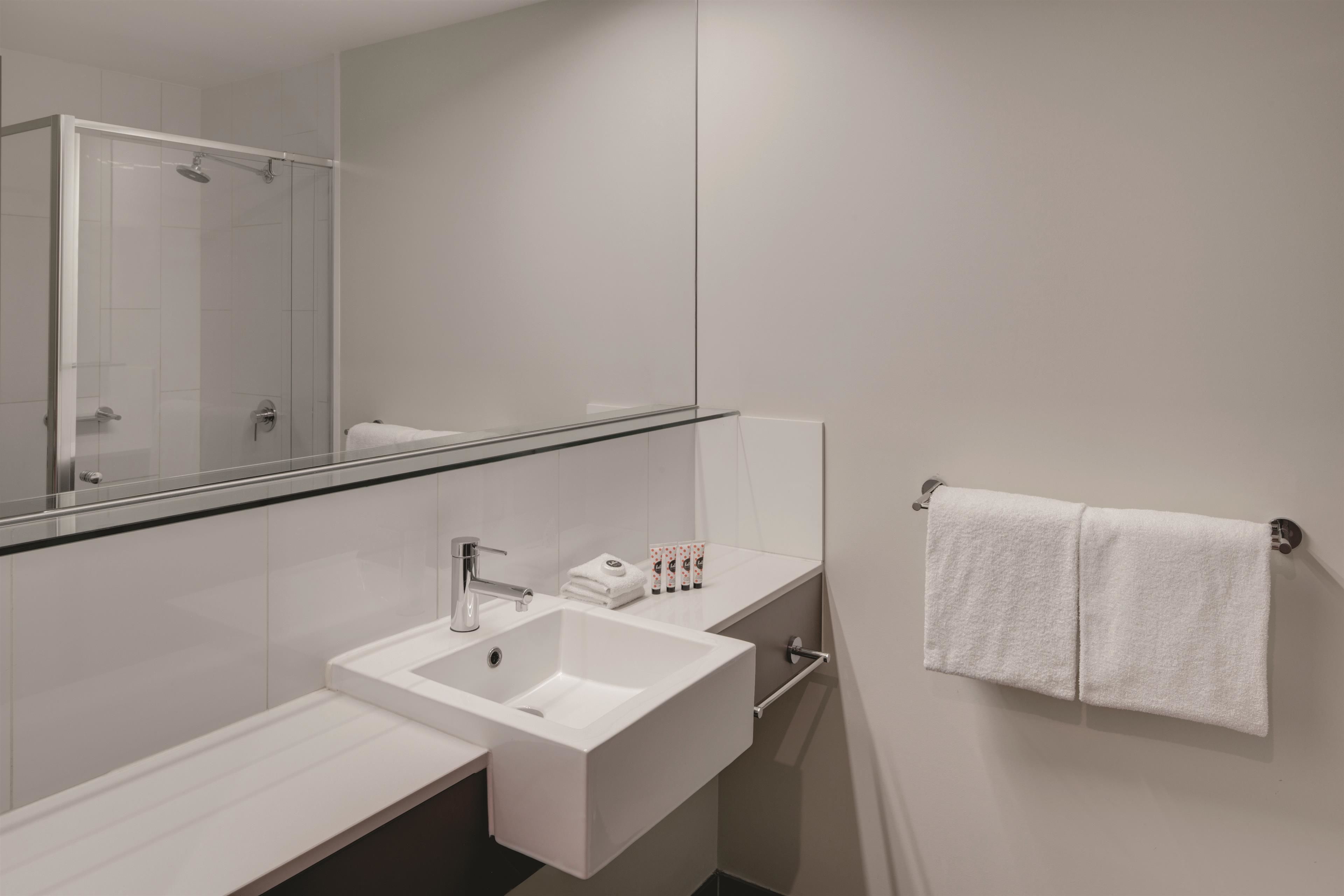 A modern bathroom with a glass-enclosed shower, a white sink, and a towel rack.