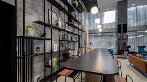 A modern interior with a long dark wooden table, black metal shelves with plants, and teal chairs.