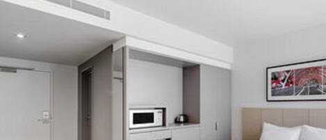 Una habitación de hotel moderna con una cama, microondas y una pequeña cocina.