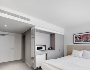 Una habitación de hotel moderna con una cama, microondas y una pequeña cocina.