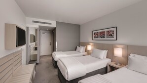 A hotel room with three beds, a TV, a wall-mounted artwork, and a bedside lamp.