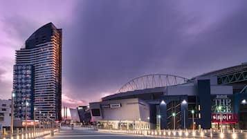 En modern arena med en stor, välvd konstruktion och en hög byggnad i bakgrunden.