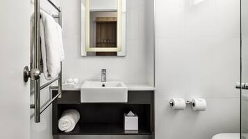 Un baño moderno con un lavabo blanco, un espejo, un perchero para toallas, un inodoro y una repisa con una caja de pañuelos.