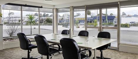 A conference room with a large table, four chairs, and large windows with a view of a parking lot and buildings.