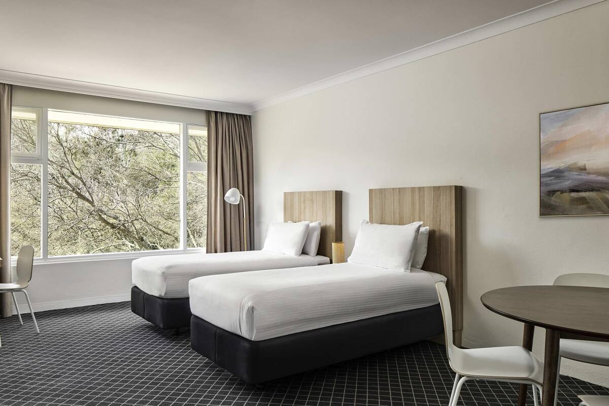 A hotel room with two beds, a desk, a chair, a lamp, and a painting on the wall.