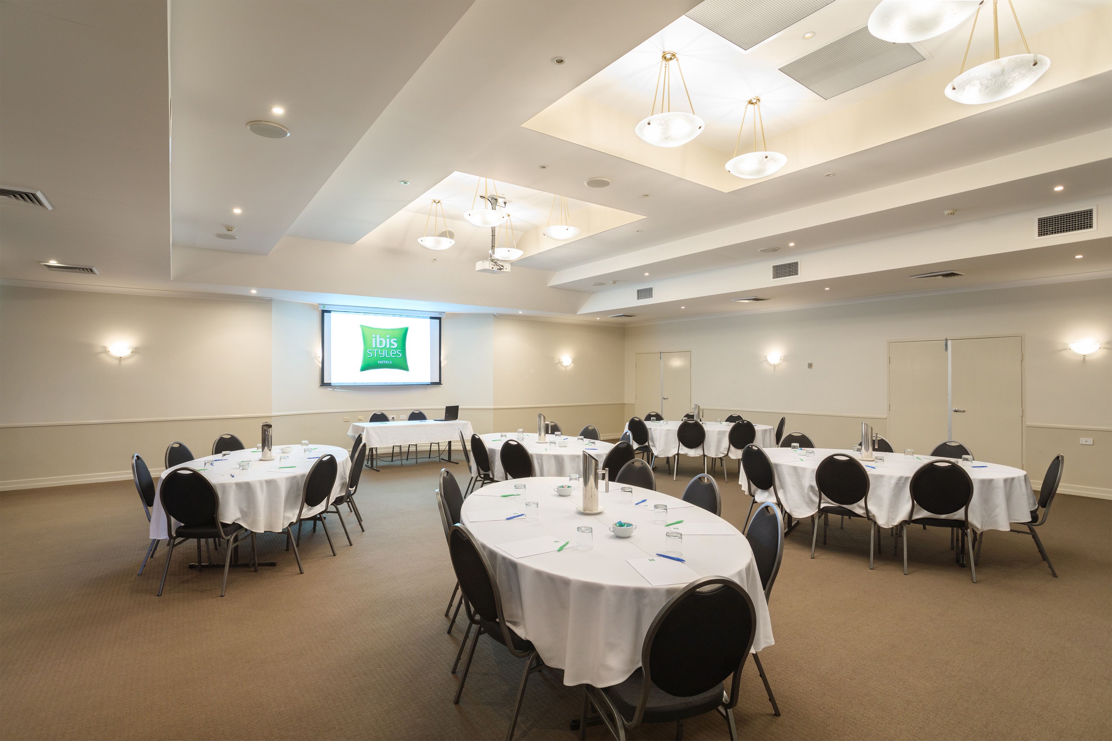 A conference room with multiple round tables, chairs, and a projector screen displaying "Gibbs Styles".